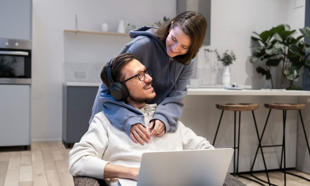A smiling young man and woman in their condo with a laptop computer